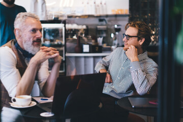 Two male professionals engaged in casual business dialogue at coffee shop, exchanging ideas and...