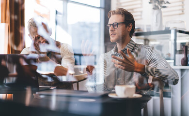 Young businessman presenting ideas with hand gestures during expressive conversation, while senior...