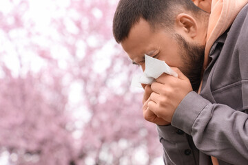 Sick young man with tissue suffering from allergy outdoors
