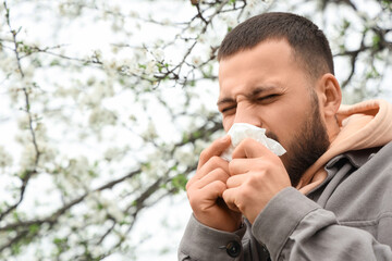 Sick young man with tissue suffering from allergy outdoors