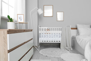 Interior of light bedroom with baby crib, lamp and blank frames