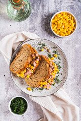 Tuna and corn salad on grain bread on a plate on a table top and vertical view