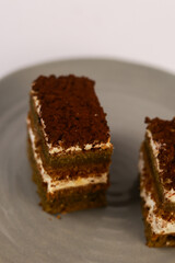 slices of layered cake featuring alternating dark spiced cake layers and creamy white frosting, artfully placed on a round grey ceramic plate. Soft overhead lighting highlights the sharp contrast