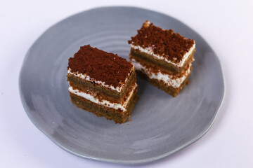 slices of layered cake featuring alternating dark spiced cake layers and creamy white frosting, artfully placed on a round grey ceramic plate. Soft overhead lighting highlights the sharp contrast