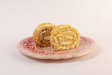 two slices of cream-filled sponge cake roll elegantly arranged on a pink decorative ceramic plate with a subtle floral pattern. Soft directional lighting accentuates the delicate spiral swirls of gol © nicholasgeorgiou