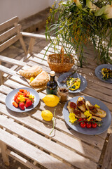 Close-up of vibrant Mediterranean brunch on a wooden table with fresh fruit, lemons, bruschetta, and olive oil. Rustic summer setting with natural light and cozy outdoor vibe