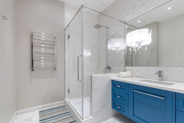 Stylish bathroom design. Glass cabin with shower. A cabinet with a blue facade and a white...