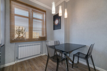 Cozy kitchen with a modern interior. Glass table with chairs made of transparent plastic. Wooden blinds on the window.
