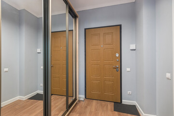An entrance hall with a brown entrance door in a small apartment. Built-in wardrobe with glass doors.