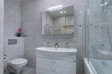 Elegant bathroom interior design. Mirrored cabinet with lighting above a white cabinet with a sink.