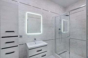 Stylish interior design of the bathroom, decorated with light gray tiles. Illuminated .mirror,...
