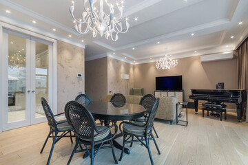 A luxurious living room in the apartment. Stylish interior with round table and chairs, Black grand piano, upholstered furniture and exclusive chandeliers.