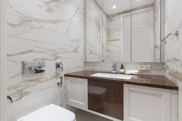 The bathroom is decorated with white marble tiles. A mirrored cabinet above a stylish cabinet with a sink.