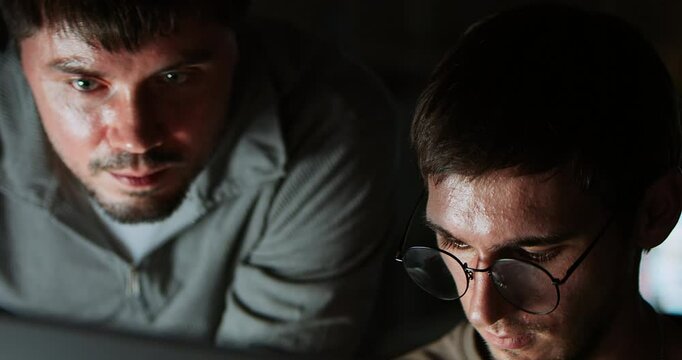 Two white Caucasian male software developers work late night on program coding, home office. People teamwork, computer engineering job, data scientist, cybersecurity, information technology. Close up
