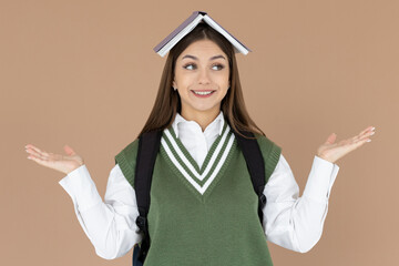 Portrait of funny young smiling student girl with an open book on her head with raised hands having...