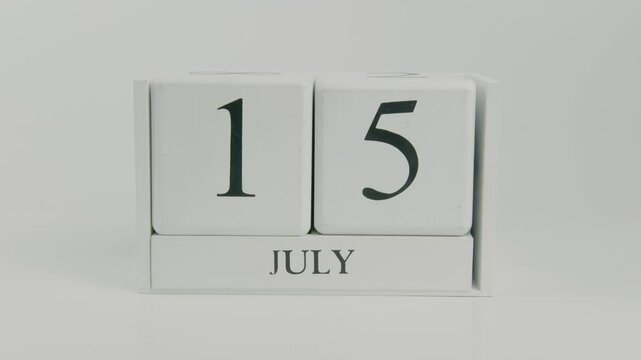 A hand flips a wooden calendar from July 15th to July 16th on a white background, marking the passage of time