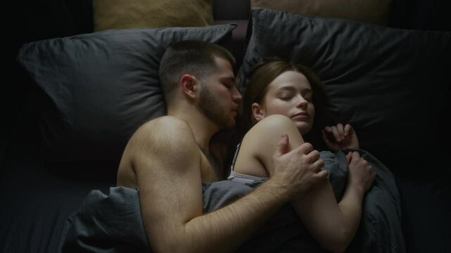 Top view shot of young newlyweds lying in bed in morning, waking up to soft daylight, man stroking shoulder of spouse, expressing deep feelings and affection