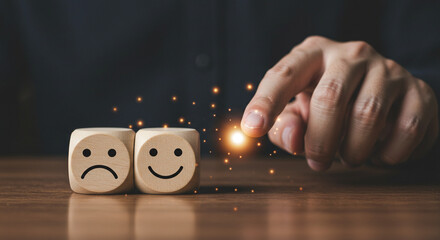 A hand selecting a happy face wooden block from a sad face block on a wooden surface with sparkles