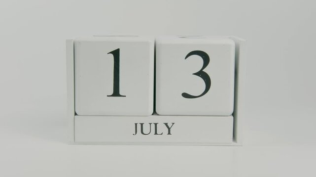 A hand flips a wooden calendar from July 13th to July 14th on a white background, marking the passage of another day