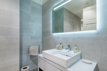 The bathroom is decorated with light tiles. Modern interior design. Illuminated mirror over the...