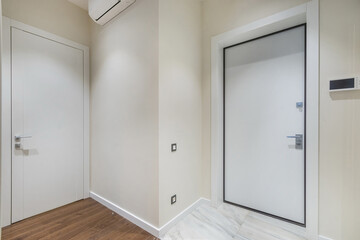A corridor with white doors in a small apartment. Light walls, laminate flooring and floor tiles.