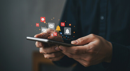 Person holding a smartphone with notification icons floating above the screen in a dark setting light