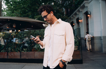 confident young professional walks along a vibrant city street, engrossed in his phone. Male...