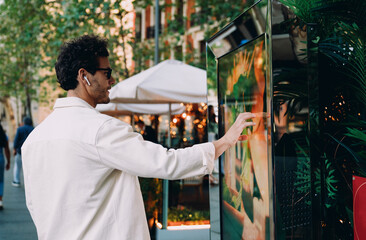 young professional uses a digital kiosk on lively city street, engaging with interactive menu.His...