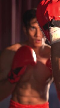 Asian and Caucasian Muay Thai boxer unleash punch in fierce boxing training session, delivering punching strike to sparring trainer, showcasing Muay Thai boxing technique and skill. Impetus