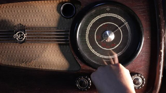  Close-up: Hand tunes knobs of an old, dusty wooden radio with analog frequency display. Evokes nostalgia, retro communication, searching for broadcasts. Ideal for historical projects.