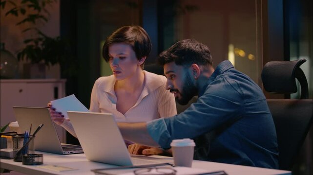 Indian businessman Caucasian businesswoman co-workers business partners man woman reading documents laptop work sad frustrated multiracial colleagues stressed paperwork problem mistake in night office