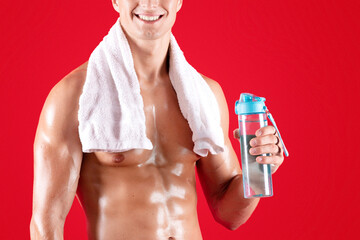 Stay hydrated during workout. Happy shirtless sportsman with towel and bottle of water on red...