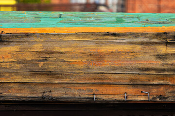 A closeup of the aged weathered wooden side of a boat with worn textures and painted green, yellow...