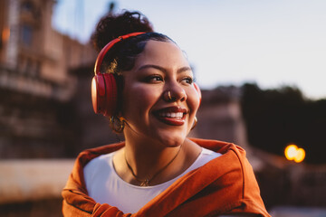 Young happy woman enjoys podcast on wireless headphones while taking in the urban night atmosphere....