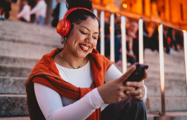 Carefree woman streams music on her smartphone, wearing wireless headphones and smiling at the...