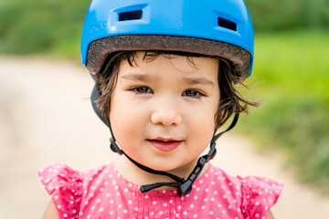 Close up portrait of toddler girl learning wearing helmet riding a bike outdoors. Concept of baby girl growing and developing