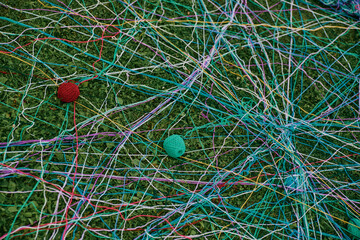 A web of multicolored threads intersects on the grass, two tangles of threads — red and blue - lie on the grass.