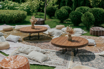 Outdoor seating area with round wooden tables, decorative vases with dried flowers, and an assortment of cushions and poufs on layered vintage rugs.
