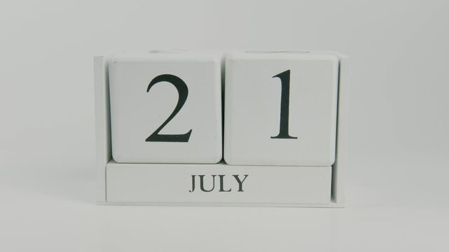 A hand flips a wooden calendar from July 21st to July 22nd on a white background, marking the transition to a new day