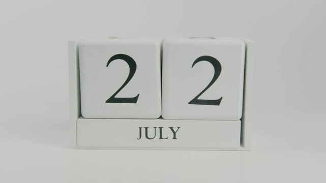 A hand flips a wooden calendar from July 22nd to July 23rd on a white background, symbolizing the change of day and the ongoing passage of time