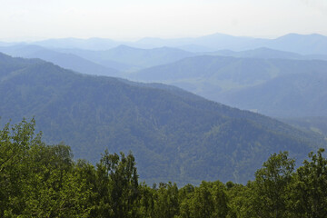 Fototapeta premium Majestic mountain scenery with rolling hills and lush greenery under a clear sky with light fog, showing the beauty of nature and the concept of traveling and hiking in the mountains