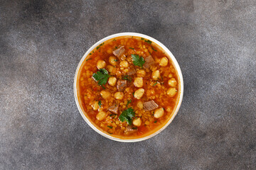 Moroccan harira soup with chickpeas, beef, parsley and spices on grey background. Top view.