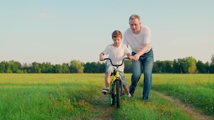 Father teaches his son child to ride bicycle in park. Child is learning to ride bike. Happy family, son dad. Child rides bicycle for first time. Boy kid dream of traveling by bike. Dad helps child.