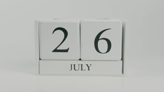 A hand flips a wooden calendar from July 26th to July 27th on a white background, marking the transition from one day to the next, a symbol of progress and time management