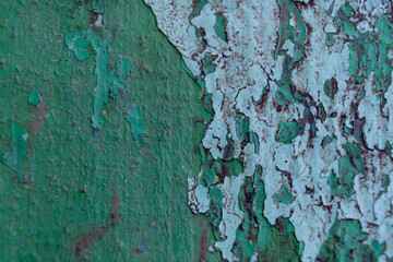 Peeling green paint reveals textured layers on weathered surface