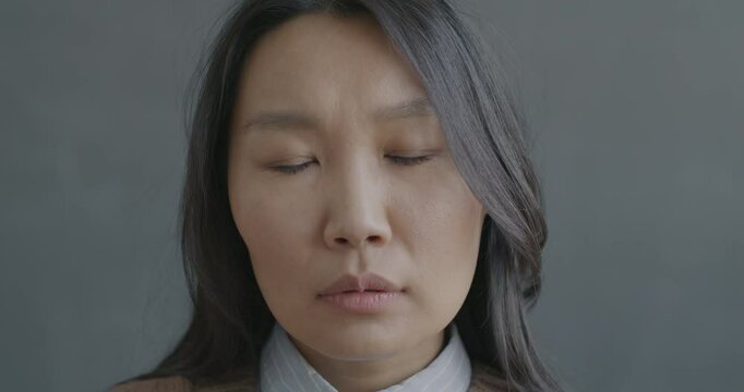 Close-up slow motion portrait of unhappy Asian woman looking at camera feeling miserable on black color background. People and negative emotion concept.