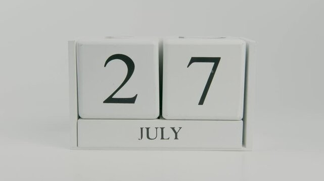 A hand flips a wooden calendar from July 27th to July 28th on a white background, representing the flow of time and the change of days