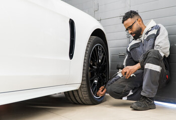 An African-American tire fitter inspects a car by measuring the tire pressure of the car. Mechanic...