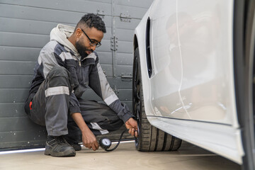 An African-American tire fitter inspects a car by measuring the tire pressure of the car. Mechanic...