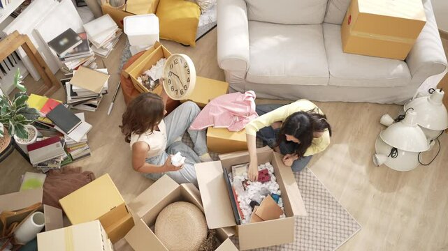Couple sitting at living room while remove furniture out from cardboard box at moving day. Top view of happy lover helping and supporting together while moving to new apartment. Relocation. Myrmidon.